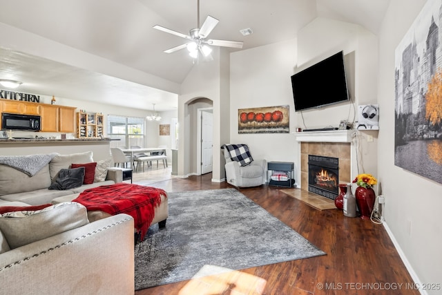 living room with a tiled fireplace, dark hardwood / wood-style floors, ceiling fan with notable chandelier, and high vaulted ceiling