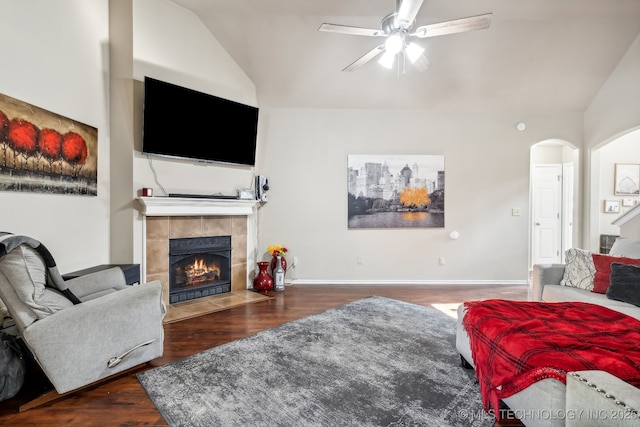 living room featuring ceiling fan, dark hardwood / wood-style flooring, a tiled fireplace, and vaulted ceiling