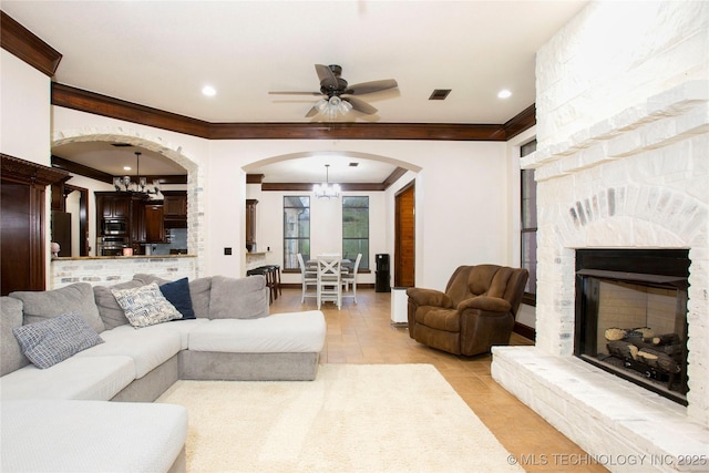 tiled living room with crown molding, a fireplace, and ceiling fan with notable chandelier