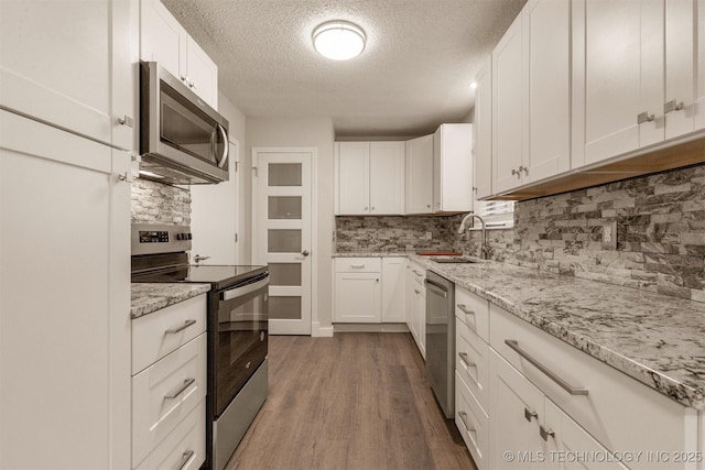 kitchen with sink, light stone counters, dark hardwood / wood-style flooring, stainless steel appliances, and white cabinets