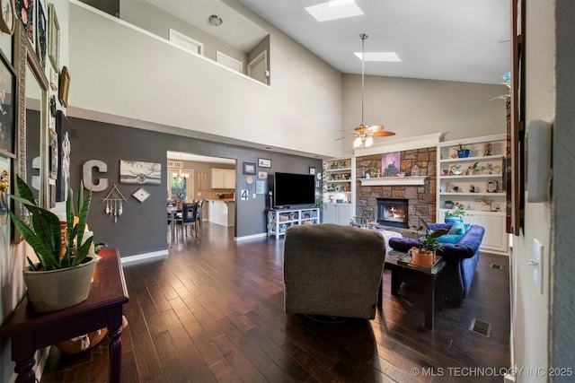 living room with lofted ceiling with skylight, a fireplace, dark hardwood / wood-style flooring, ceiling fan, and built in shelves