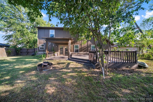 back of property with a wooden deck, an outdoor fire pit, french doors, and a lawn