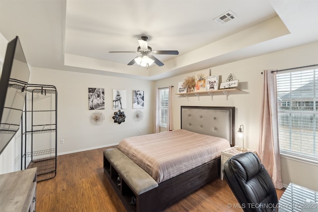 bedroom with a tray ceiling, dark wood-type flooring, and ceiling fan