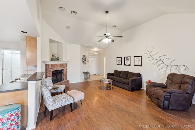 living room with high vaulted ceiling, a brick fireplace, hardwood / wood-style floors, and ceiling fan