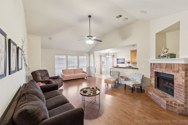 living room featuring hardwood / wood-style flooring, ceiling fan with notable chandelier, high vaulted ceiling, and a brick fireplace