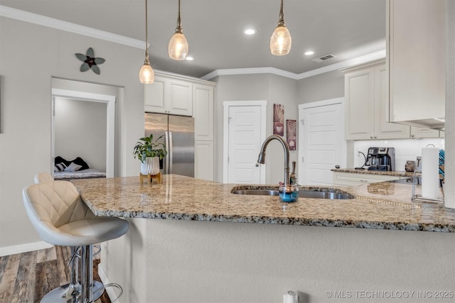 kitchen with sink, light stone counters, crown molding, decorative light fixtures, and stainless steel fridge