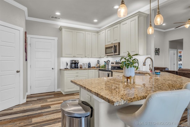 kitchen featuring crown molding, stainless steel appliances, a kitchen breakfast bar, light stone countertops, and decorative light fixtures