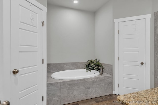 bathroom with tiled tub and wood-type flooring