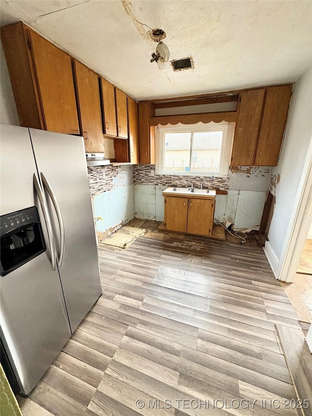 kitchen with stainless steel refrigerator with ice dispenser, sink, a textured ceiling, light hardwood / wood-style floors, and backsplash