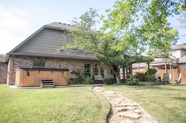 back of house featuring a hot tub and a lawn