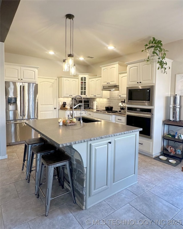 kitchen featuring white cabinetry, appliances with stainless steel finishes, an island with sink, and decorative backsplash