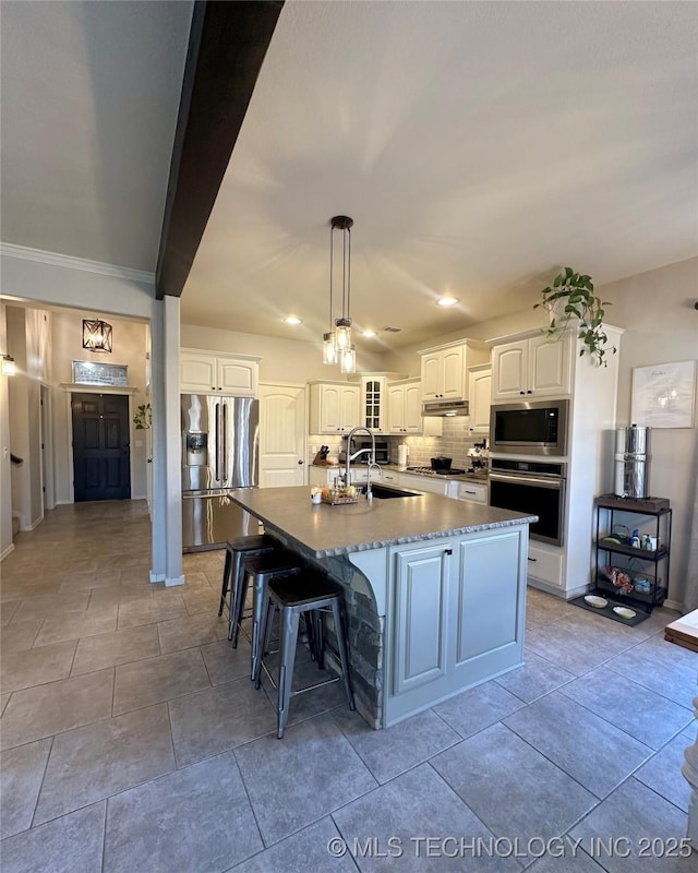 kitchen featuring sink, white cabinetry, stainless steel appliances, tasteful backsplash, and an island with sink