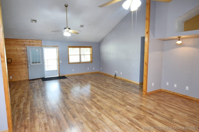 spare room featuring lofted ceiling, wood-type flooring, wooden walls, and ceiling fan