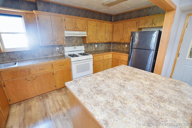 kitchen featuring white gas stove, stainless steel fridge, and light hardwood / wood-style floors