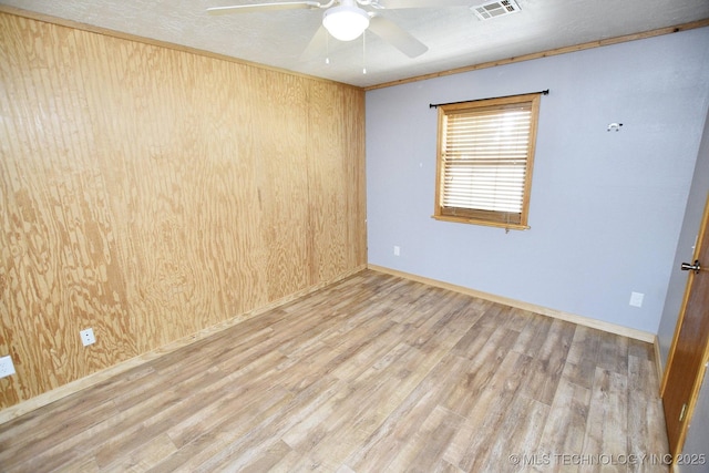 spare room with wood walls, a textured ceiling, ceiling fan, and light hardwood / wood-style flooring