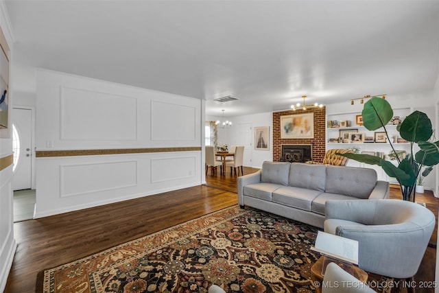 living room featuring a brick fireplace, dark wood-type flooring, and a notable chandelier