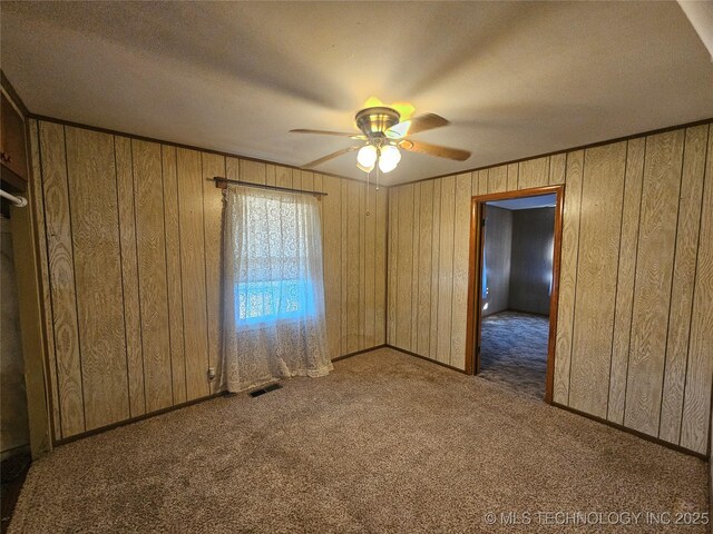 empty room featuring ceiling fan, wooden walls, and dark carpet