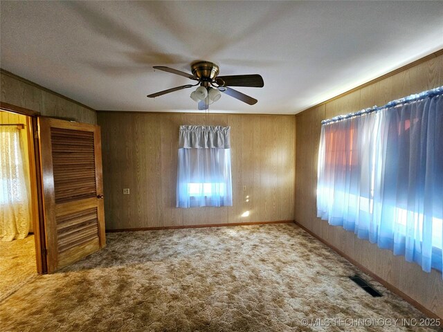 spare room featuring crown molding, wooden walls, ceiling fan, and carpet