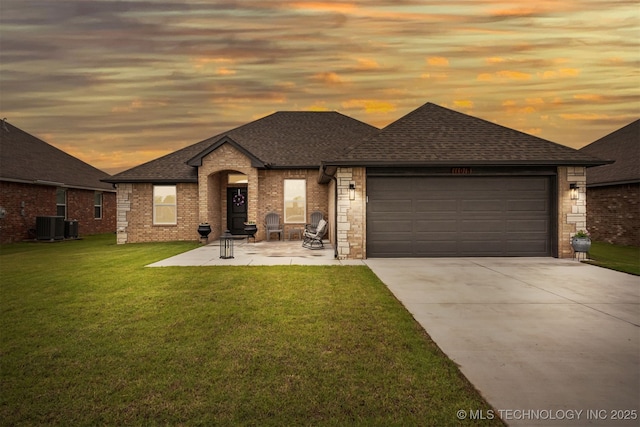 view of front of home featuring a garage, a yard, and central AC