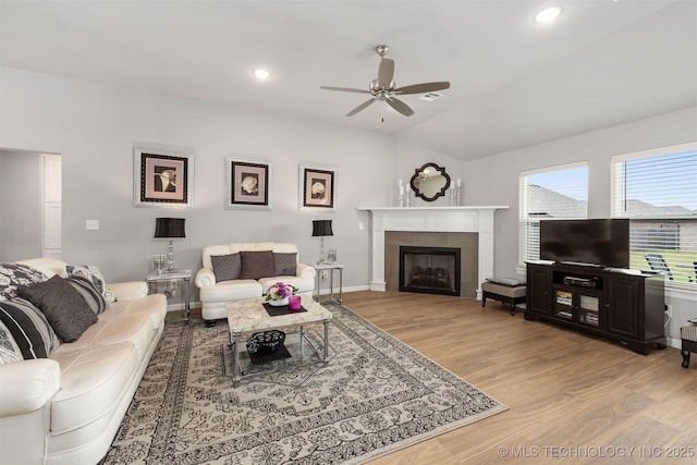 living room featuring ceiling fan, wood-type flooring, a tiled fireplace, and vaulted ceiling