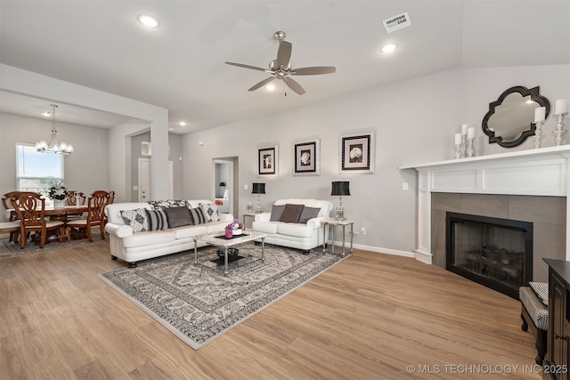 living room with ceiling fan with notable chandelier, a fireplace, and light hardwood / wood-style floors