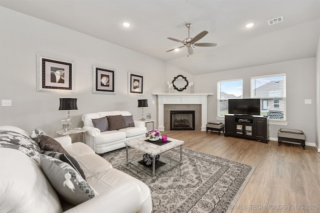 living room with a tiled fireplace, wood-type flooring, ceiling fan, and vaulted ceiling