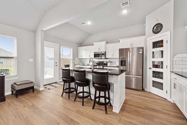 kitchen featuring vaulted ceiling, tasteful backsplash, white cabinetry, an island with sink, and stainless steel appliances