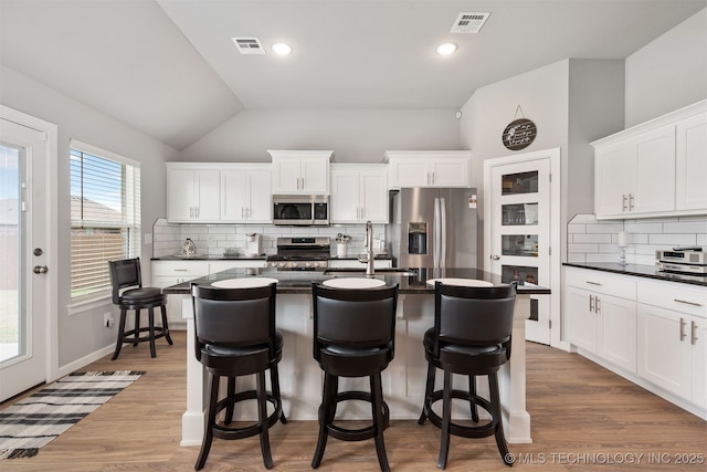 kitchen with an island with sink, appliances with stainless steel finishes, hardwood / wood-style floors, and white cabinets