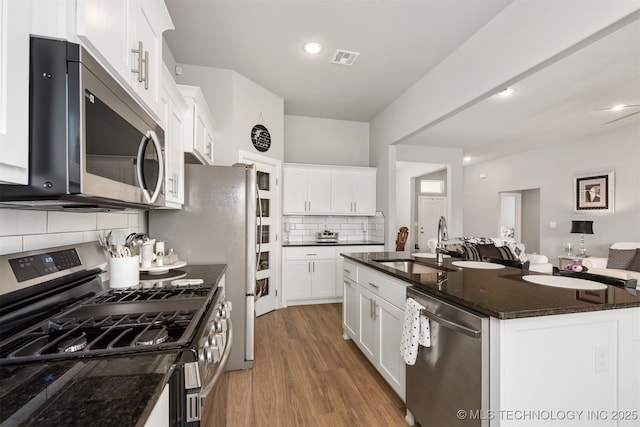 kitchen featuring appliances with stainless steel finishes, an island with sink, sink, white cabinets, and dark stone counters