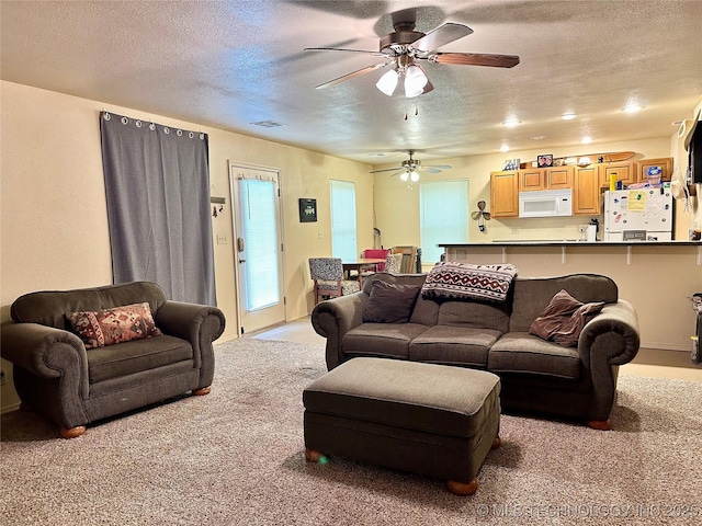 living room featuring ceiling fan, light carpet, and a textured ceiling