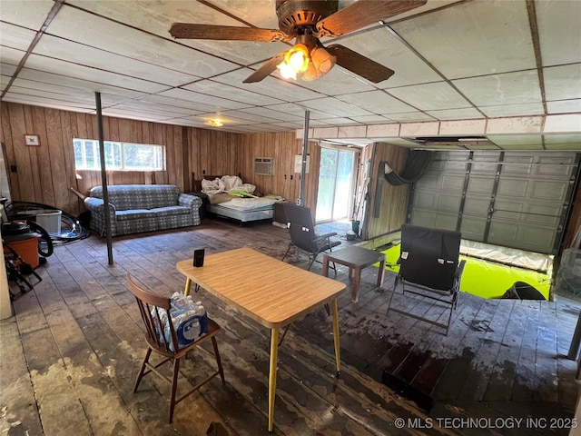 interior space featuring ceiling fan, hardwood / wood-style floors, a drop ceiling, an AC wall unit, and wood walls