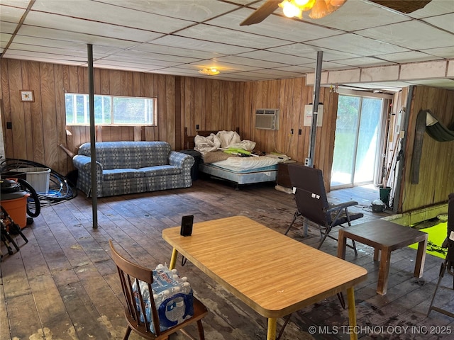 living room featuring dark wood-type flooring, ceiling fan, a wall mounted air conditioner, a drop ceiling, and wood walls