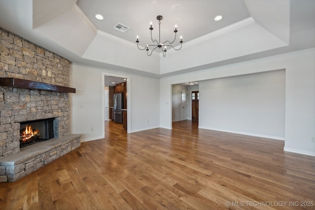 unfurnished living room featuring a raised ceiling, wood-type flooring, a stone fireplace, and an inviting chandelier