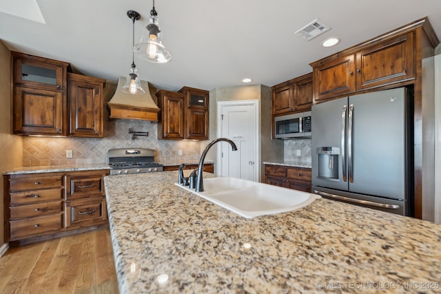 kitchen with stainless steel appliances, premium range hood, sink, and light stone counters