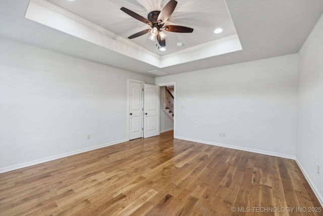 empty room with crown molding, hardwood / wood-style flooring, a raised ceiling, and ceiling fan