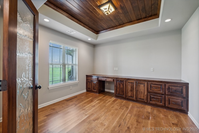 unfurnished office with light hardwood / wood-style flooring, built in desk, wooden ceiling, and a tray ceiling