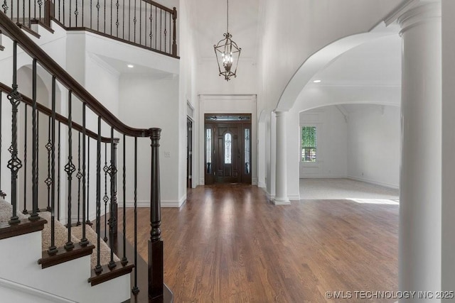 foyer entrance with ornate columns, a notable chandelier, wood-type flooring, and a high ceiling