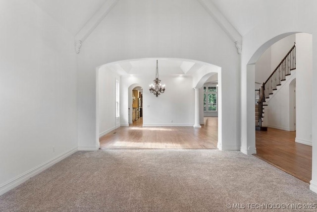 unfurnished living room featuring light carpet, high vaulted ceiling, and an inviting chandelier