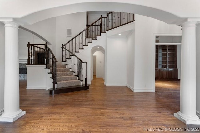 entrance foyer featuring a towering ceiling, dark hardwood / wood-style floors, and ornate columns