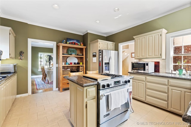 kitchen with dark stone countertops, crown molding, stainless steel appliances, and cream cabinetry