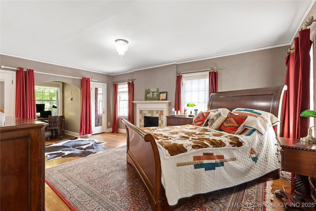 bedroom featuring multiple windows, a tiled fireplace, and light hardwood / wood-style floors