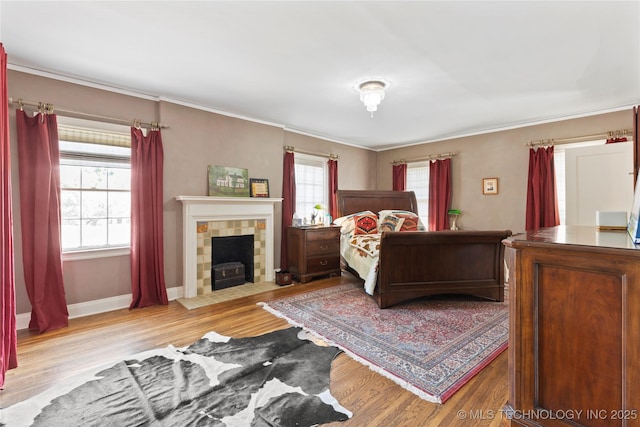 bedroom featuring multiple windows, a tile fireplace, ornamental molding, and light wood-type flooring