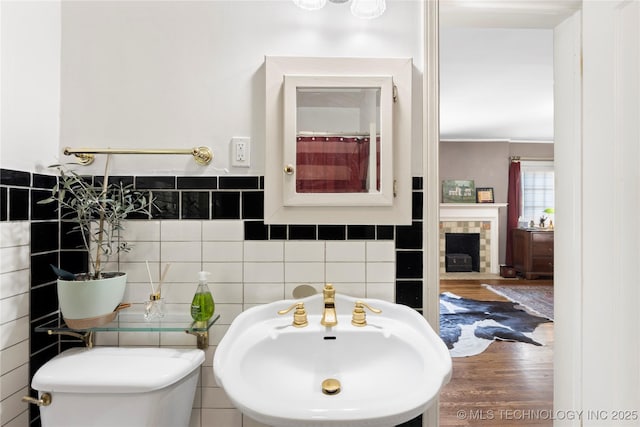 bathroom featuring sink, a tile fireplace, tile walls, hardwood / wood-style floors, and toilet