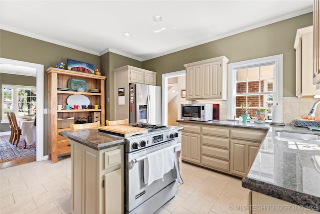 kitchen featuring sink, dark stone countertops, a center island, stainless steel appliances, and cream cabinets