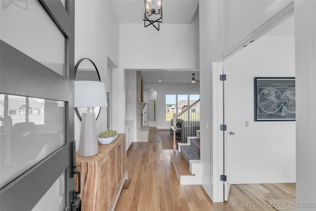 foyer entrance with a towering ceiling, ceiling fan with notable chandelier, and light hardwood / wood-style floors