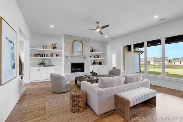 living room featuring a large fireplace, built in features, ceiling fan, and light hardwood / wood-style flooring