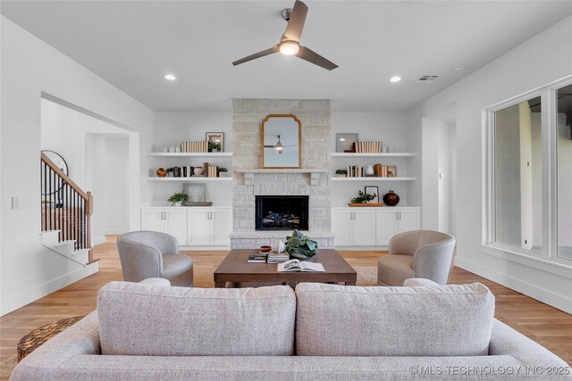 living room with built in features, ceiling fan, a fireplace, and light wood-type flooring