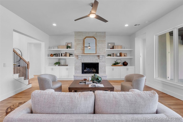 living room with ceiling fan, built in features, a fireplace, and light hardwood / wood-style flooring