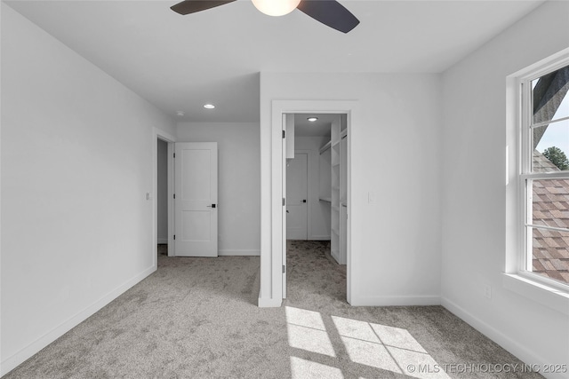 unfurnished bedroom with a spacious closet, light carpet, ceiling fan, and a closet