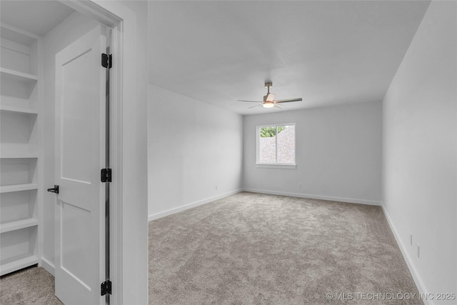 unfurnished room with built in shelves, light colored carpet, and ceiling fan